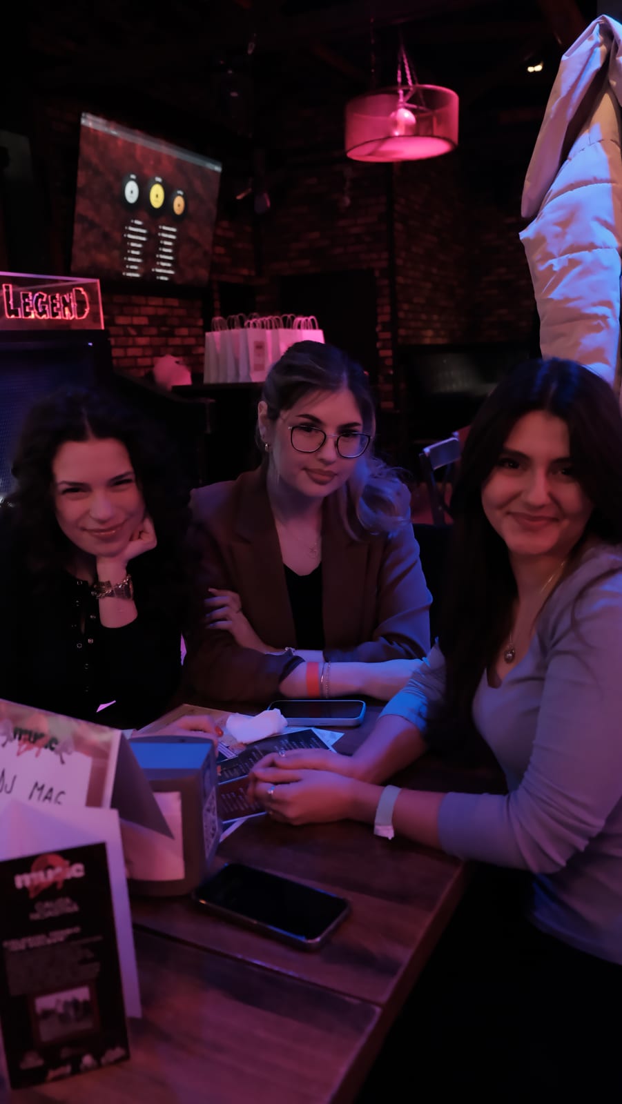 Trei participante zâmbind la o masă, cu biletele Music Bingo în față